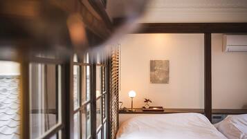 A hotel room with a bed, a bedside table with a lamp, a wall-mounted air conditioner, and a window with blinds.