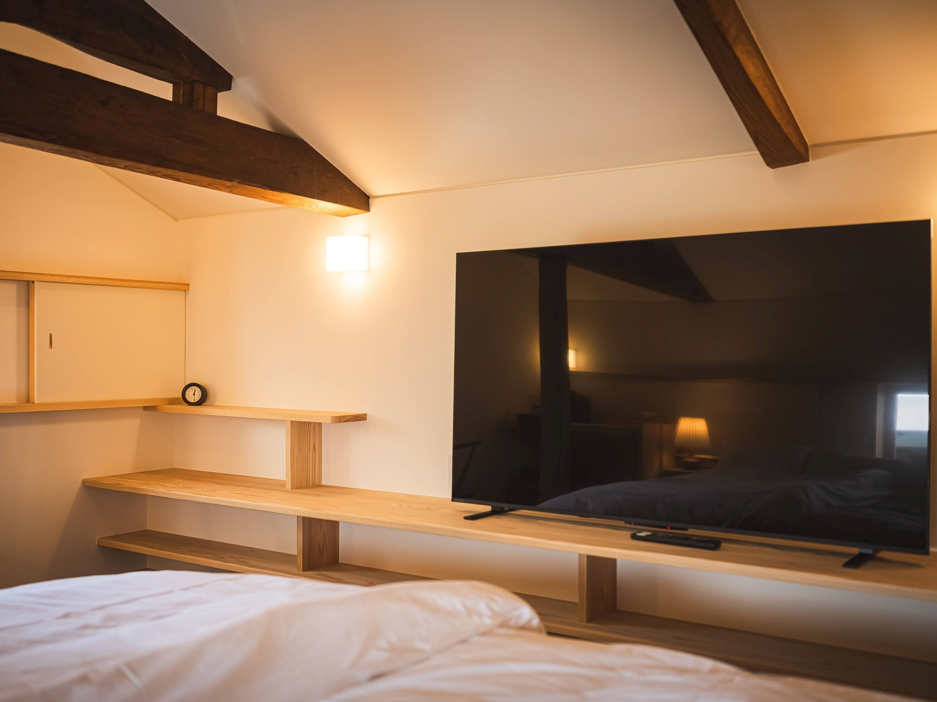 A bedroom with a bed, a TV, a shelf, and a clock.