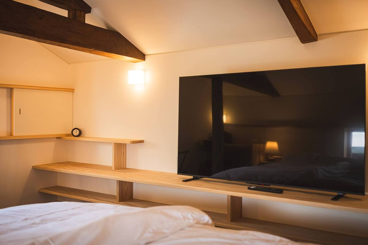 A bedroom with a bed, a TV, a shelf, and a clock.