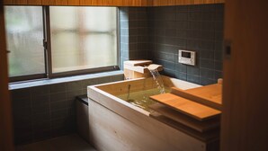 A wooden bathtub with a faucet, a window, and a wall-mounted microwave. - UCHIKO-Inn (Uchiko)