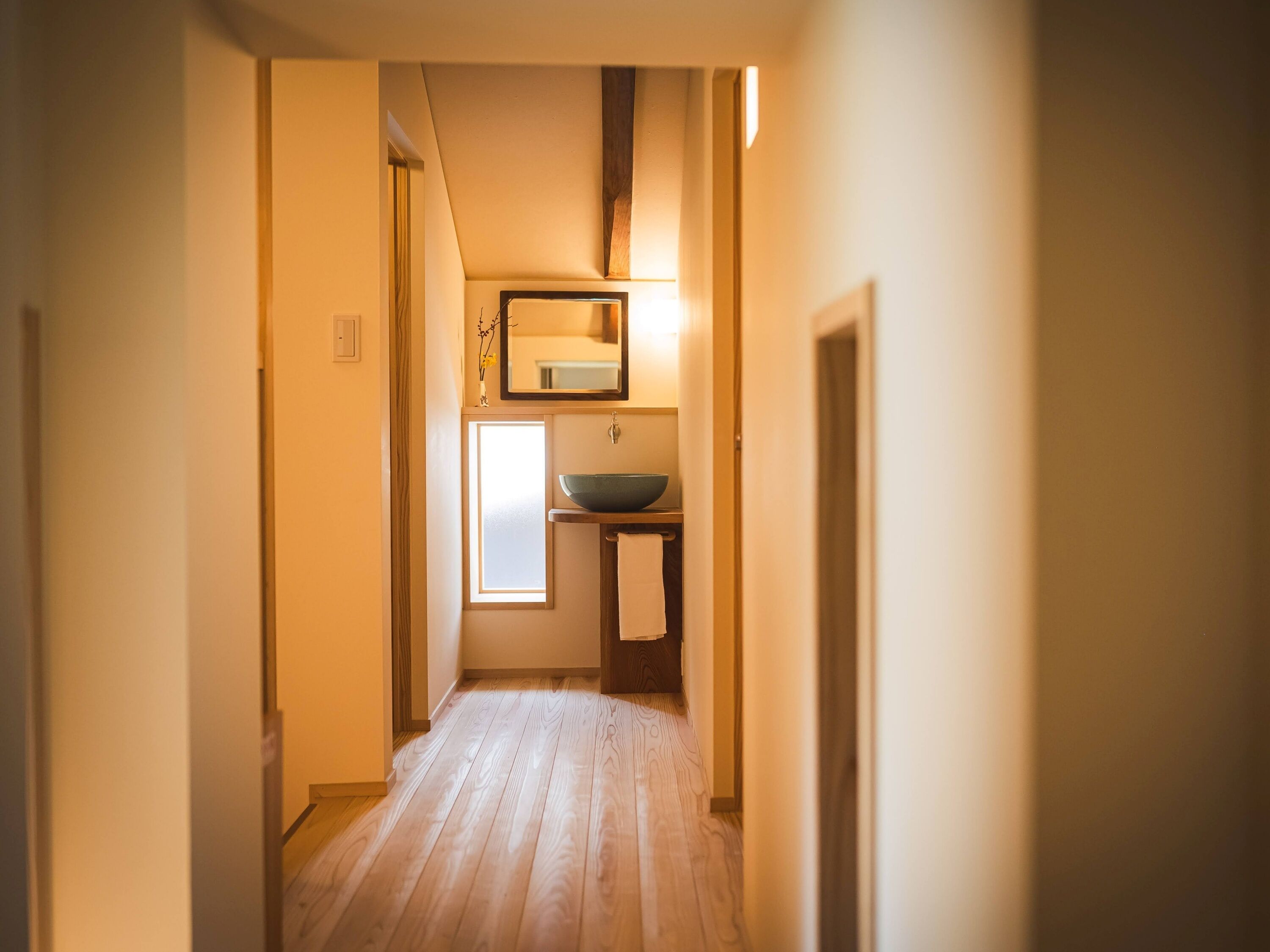 A narrow hallway with wooden flooring, a small sink, and a mirror above it.