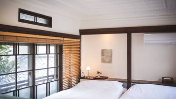 A hotel room with a large window, a bed, a bedside table with a lamp, and an air conditioning unit.