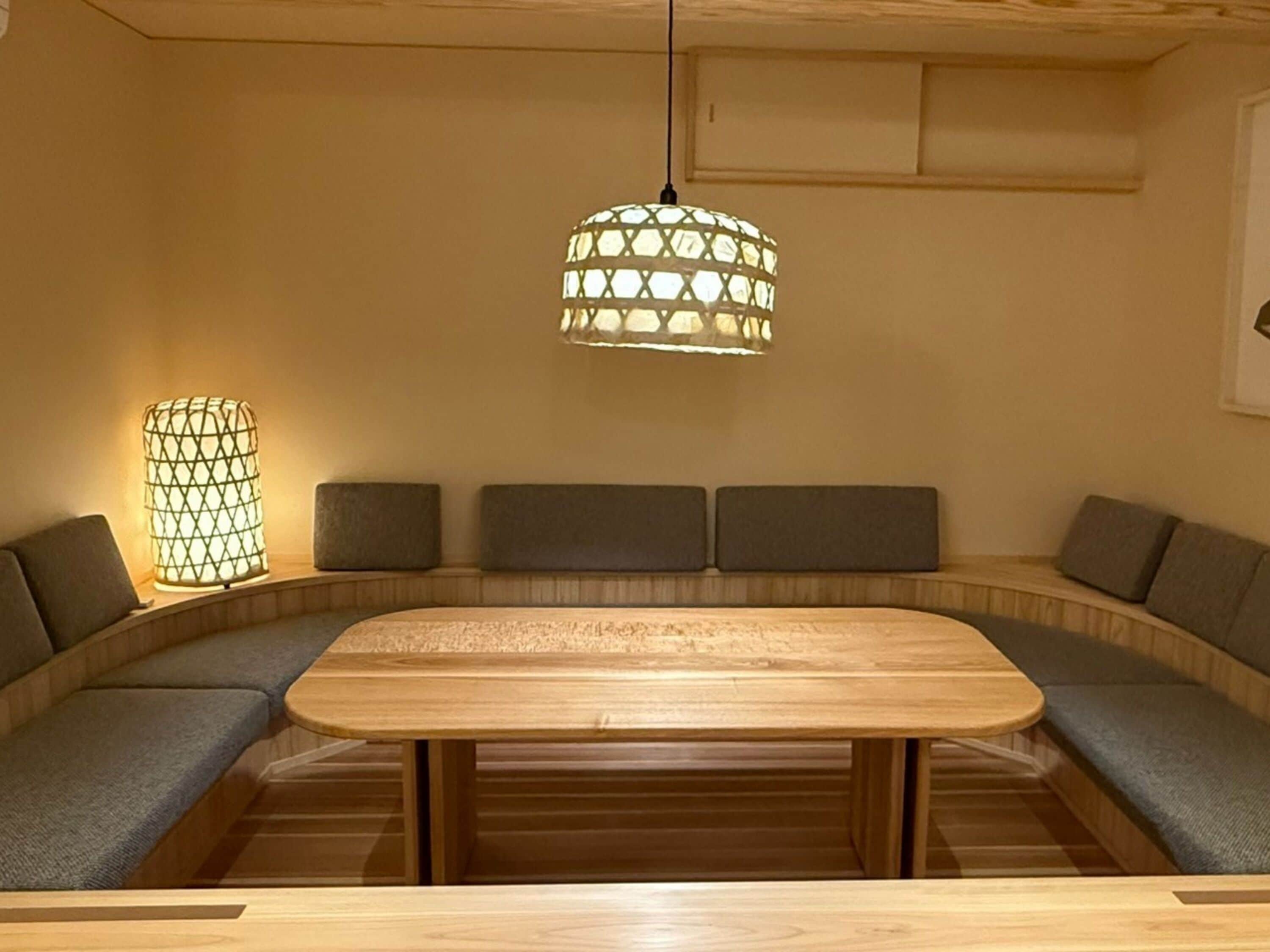 A wooden dining table with a bench around it, a hanging light fixture, and a wall-mounted shelf.