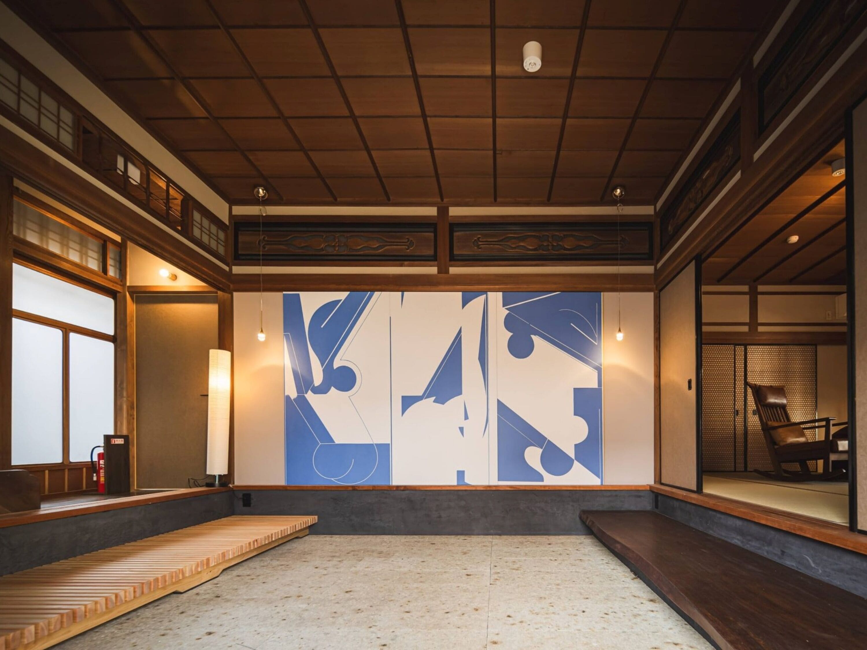 Una habitación japonesa tradicional con suelo de tatami, un banco de madera bajo y un cuadro abstracto grande en la pared.