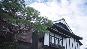 Il s’agit d’un bâtiment japonais traditionnel, doté d’une structure en bois, d’un toit recouvert de tuiles et d’un grand arbre qui se trouve devant.