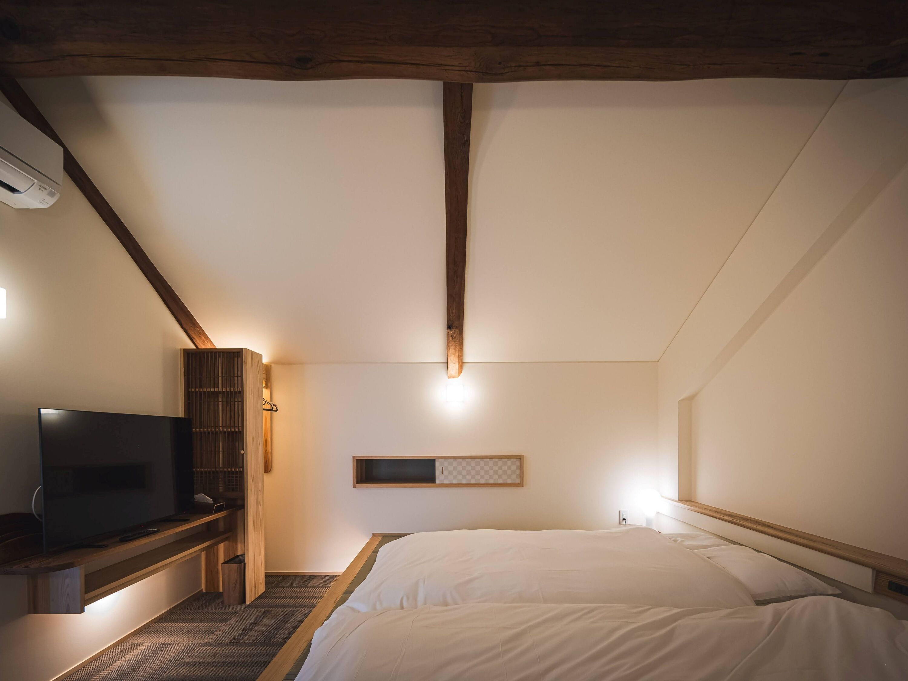 A bedroom with a bed, a TV, a wooden cabinet, and a ceiling with exposed beams.