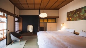 A traditional Japanese-style bedroom with tatami flooring, a bed, a chair, and a large painting on the wall. - UCHIKO-Inn (Uchiko)