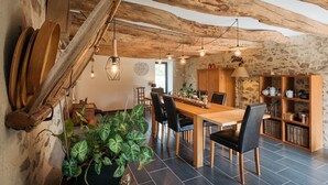 A rustic dining area with a wooden table, chairs, and a stone wall. - Le Champ Bagnolet (Voussac)