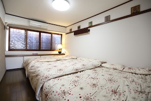 Un dormitorio con una cama grande, una ventana con vistas, una mesita de noche con una lámpara y una estantería con fotografías.
