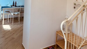 Zona pranzo con tavolo apparecchiato per due, orologio a parete e scala con ringhiera in legno.