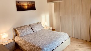 Una camera da letto con un letto, comodini, una lampada a sospensione, un'armadio in legno e un quadro appeso al muro.
