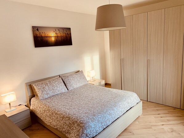 A bedroom with a bed, bedside tables, a hanging lamp, a wooden wardrobe, and a wall-mounted picture.