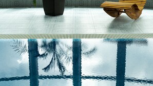 A swimming pool with clear water and visible lane markings, a wooden bench, and a textured wall in the background. - Hotel Kristály (Ajka)