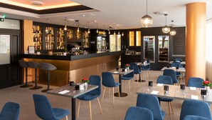 A modern restaurant with a bar area, blue upholstered chairs, and a bar counter with various bottles. - Hotel Kristály (Ajka)
