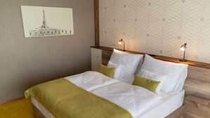 A neatly made bed with white and green bedding, two bedside lamps, and a wall-mounted picture of a building. - Hotel Kristály (Ajka)