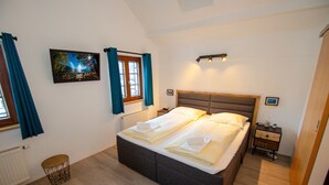 Ein Schlafzimmer mit einem großen Bett, einem Nachttisch, einem Beistelltisch, einem Bild an der Wand und einem Fenster mit Vorhängen.