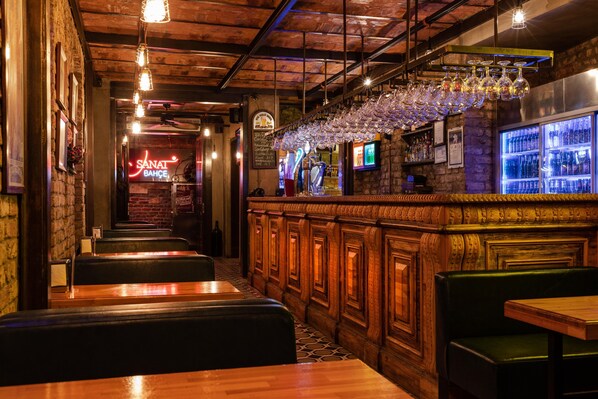 A bar area with wooden booths, a neon sign, and a bar counter with hanging glasses. - Sanat Hostel Taksim (Istanbul)