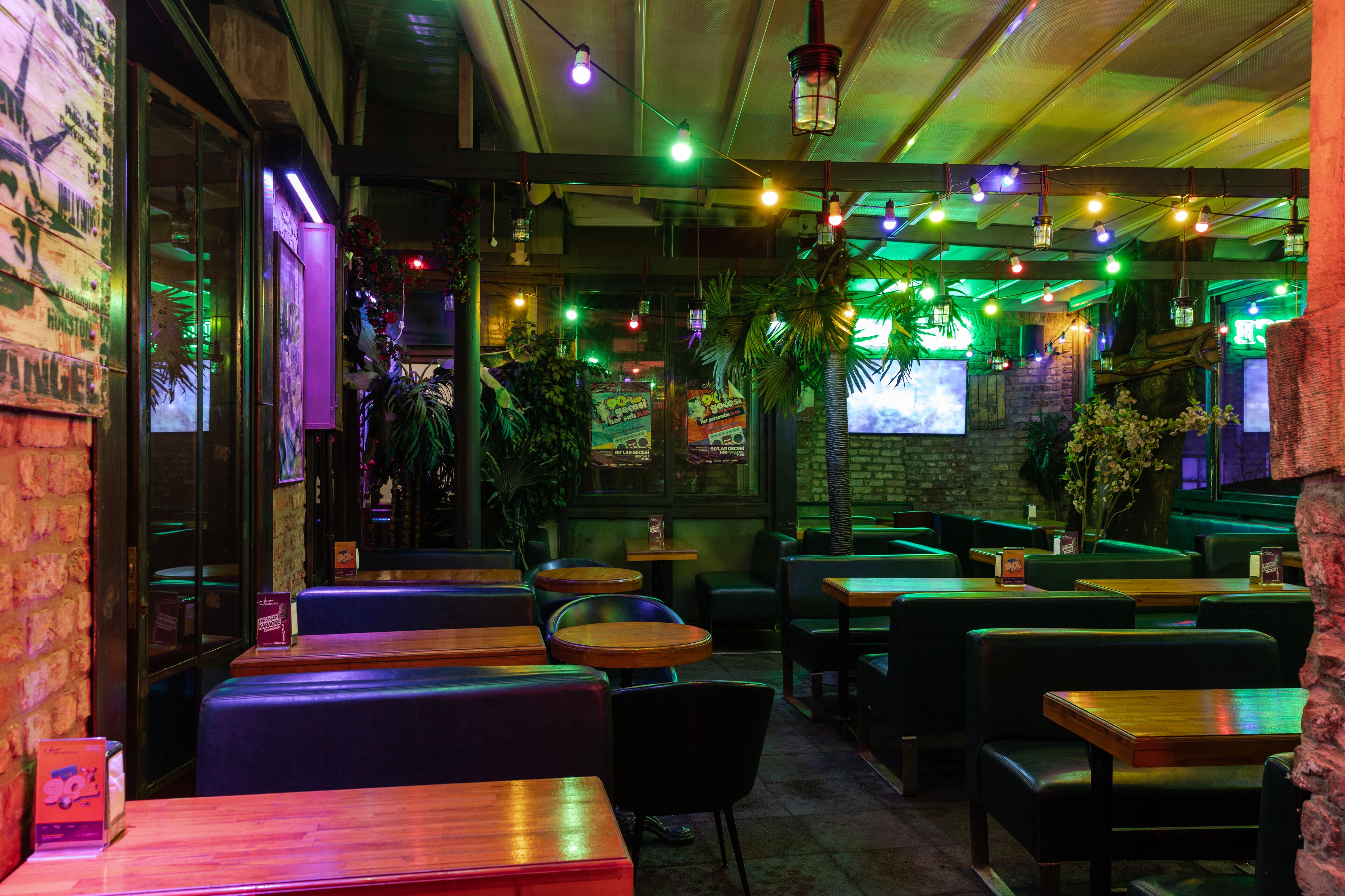 Un ristorante con posti a sedere a isola e tavoli, illuminazione soffusa verde e piante decorative.