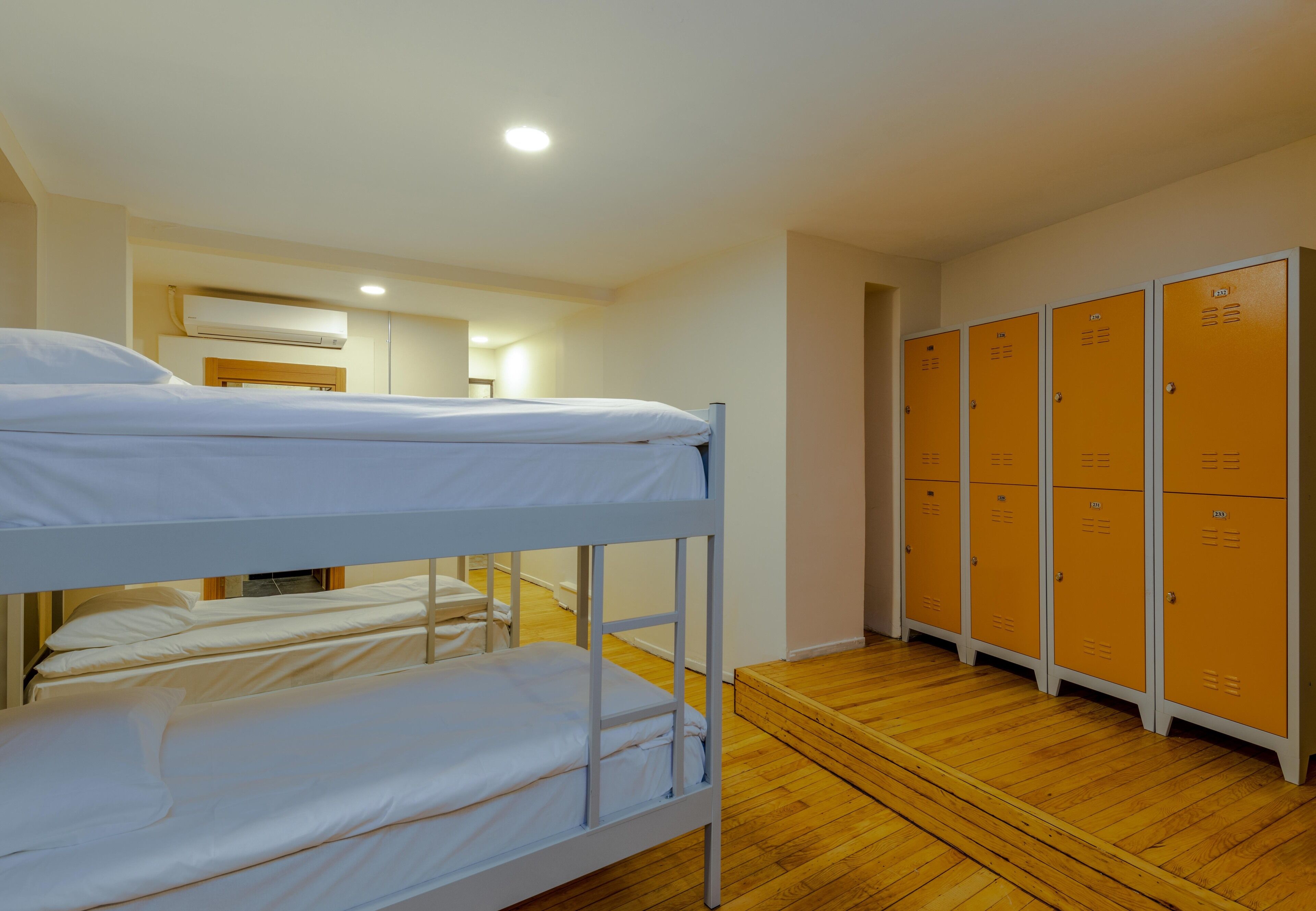 A bunk bed room with wooden flooring, a white ceiling, and a row of orange lockers.