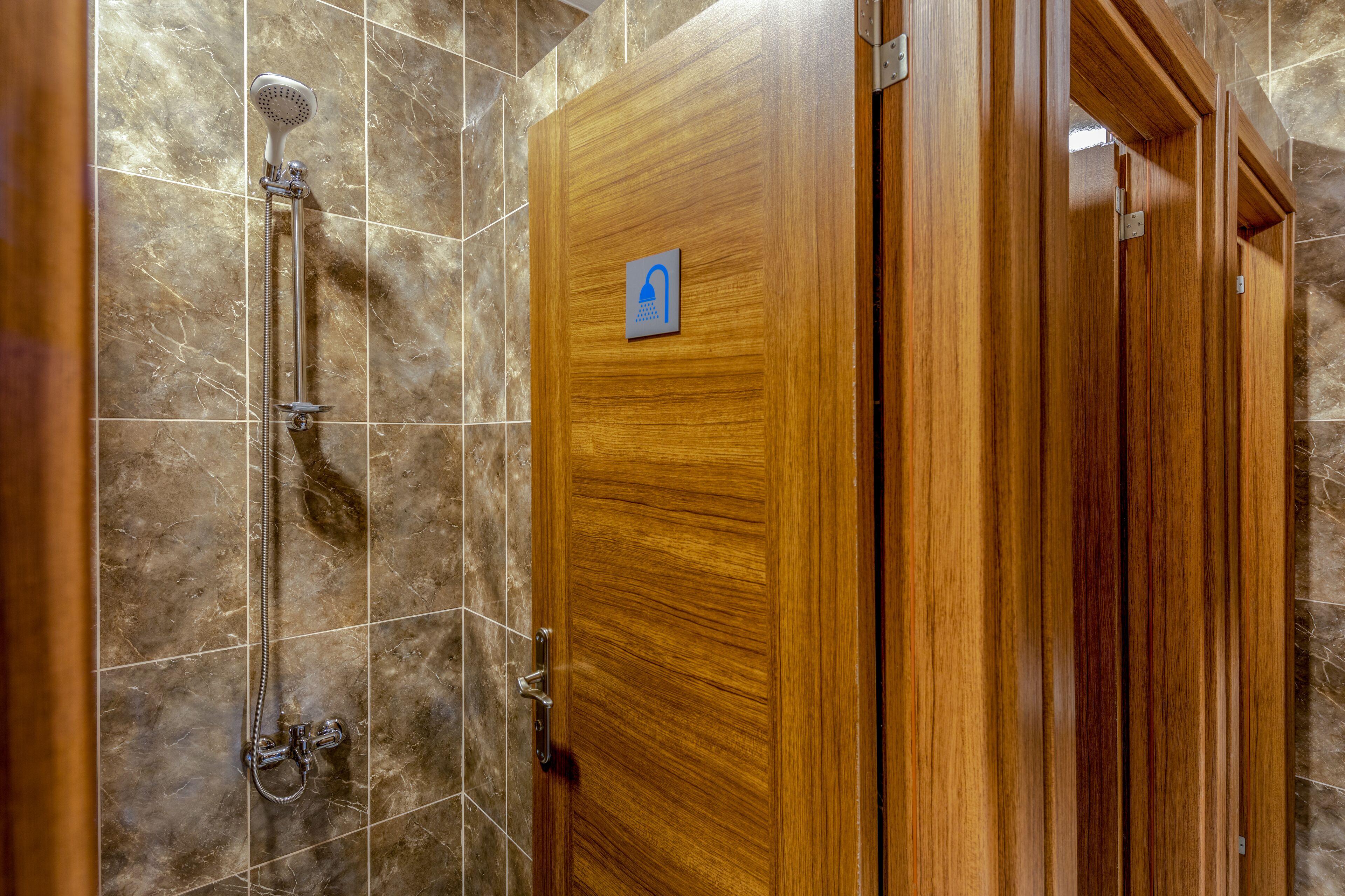 A wooden door with a blue handicap accessibility sign, a shower with a handheld showerhead, and a tiled wall.