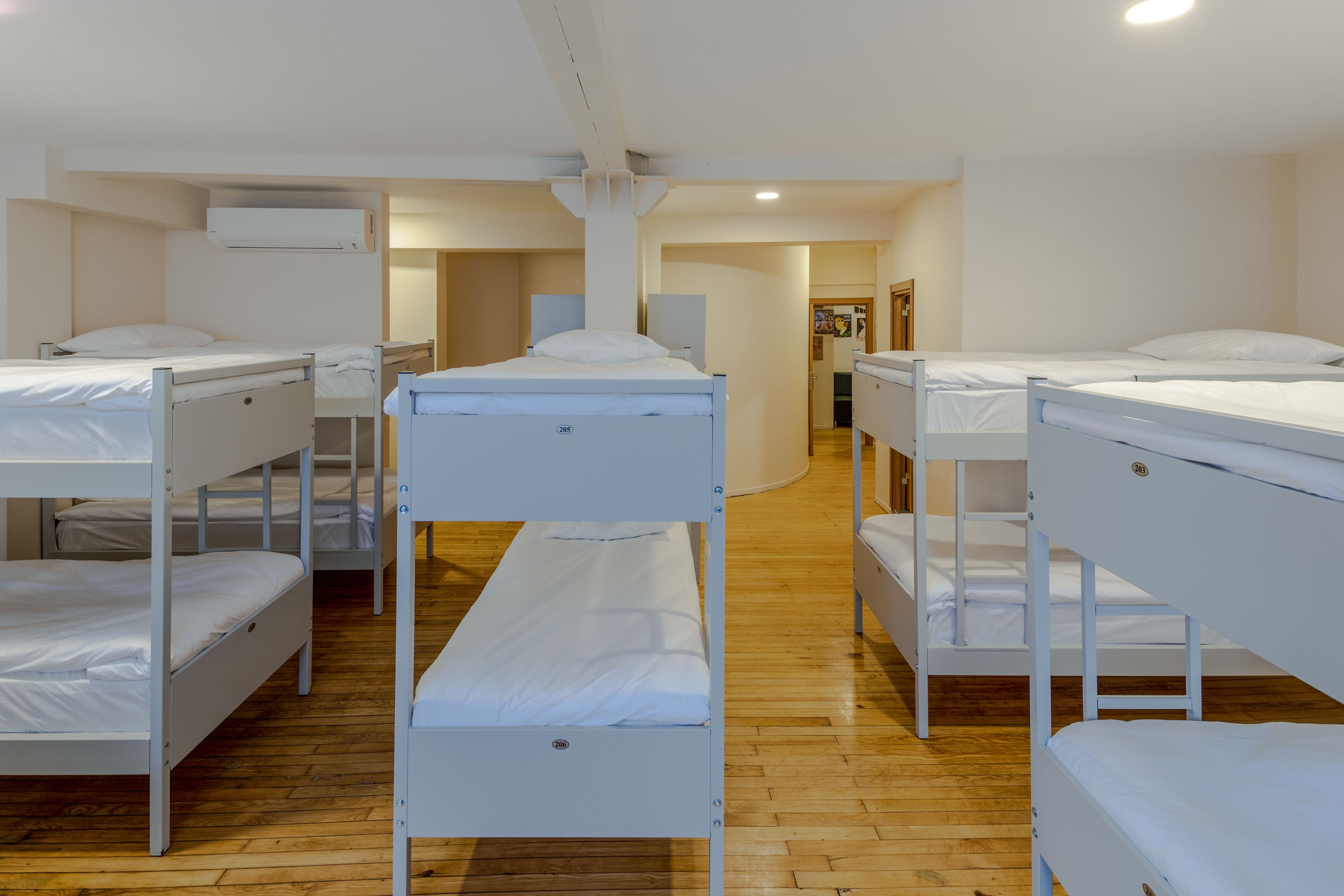 A room with bunk beds arranged in two rows, wooden flooring, and a white color scheme.