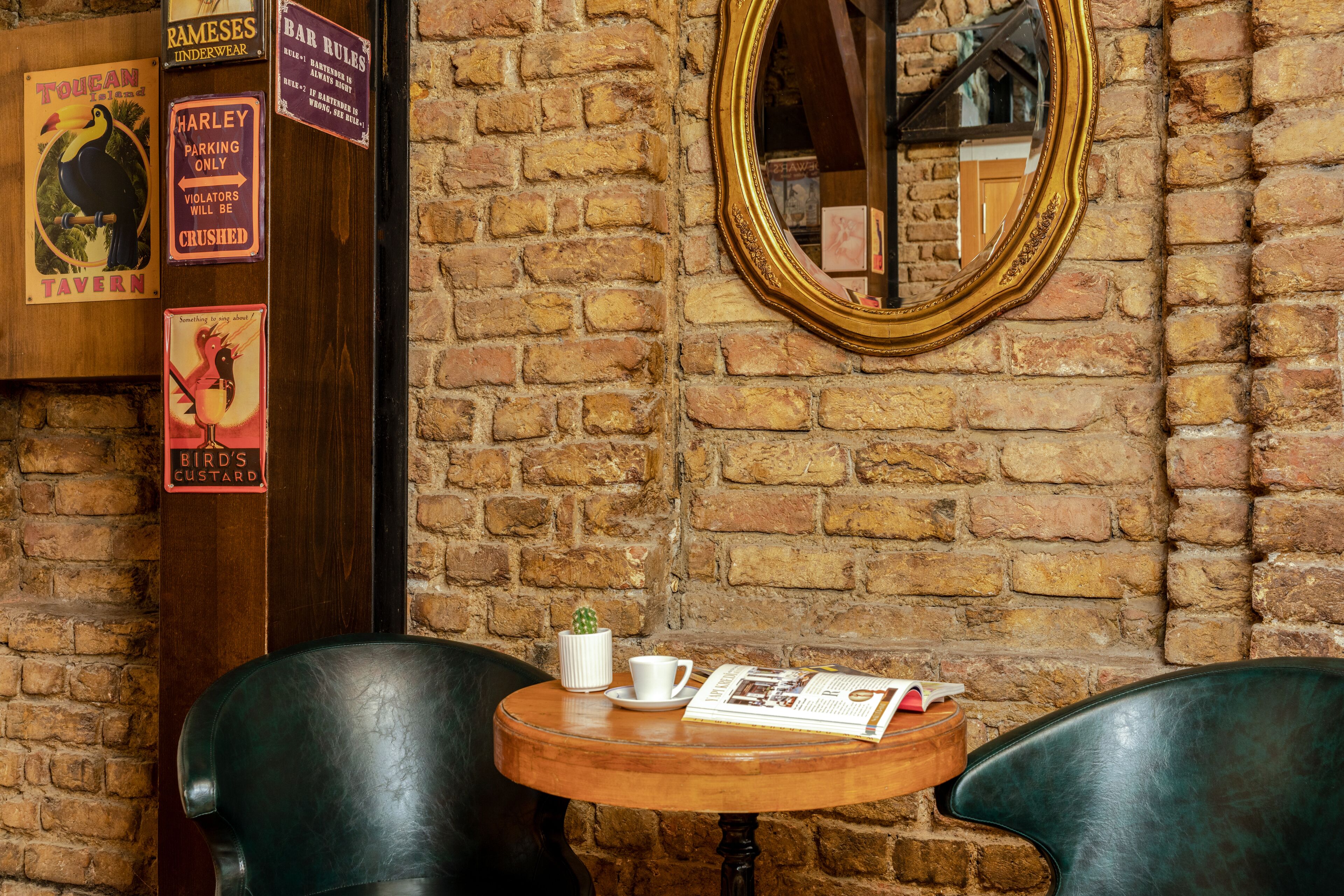 A brick wall with a mirror and various signs, including a bird's custard sign.