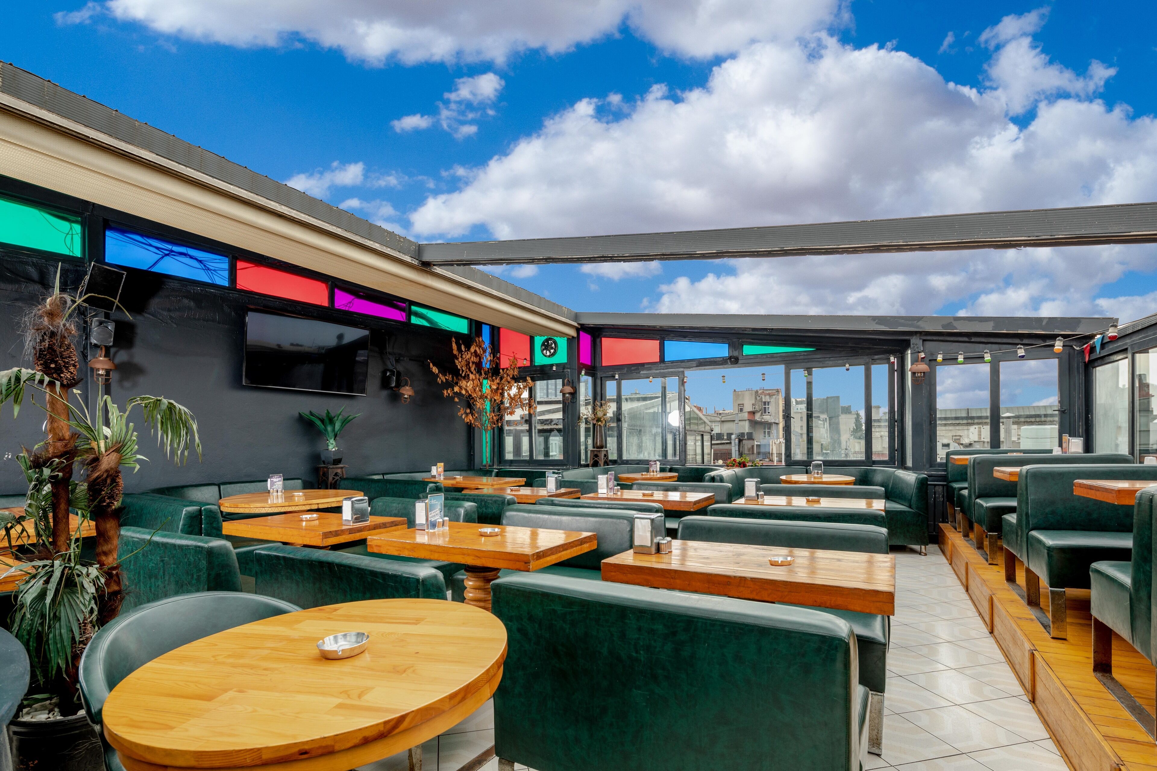 Un restaurante en la azotea con asientos verdes, ventanas amplias y vistas a la ciudad.