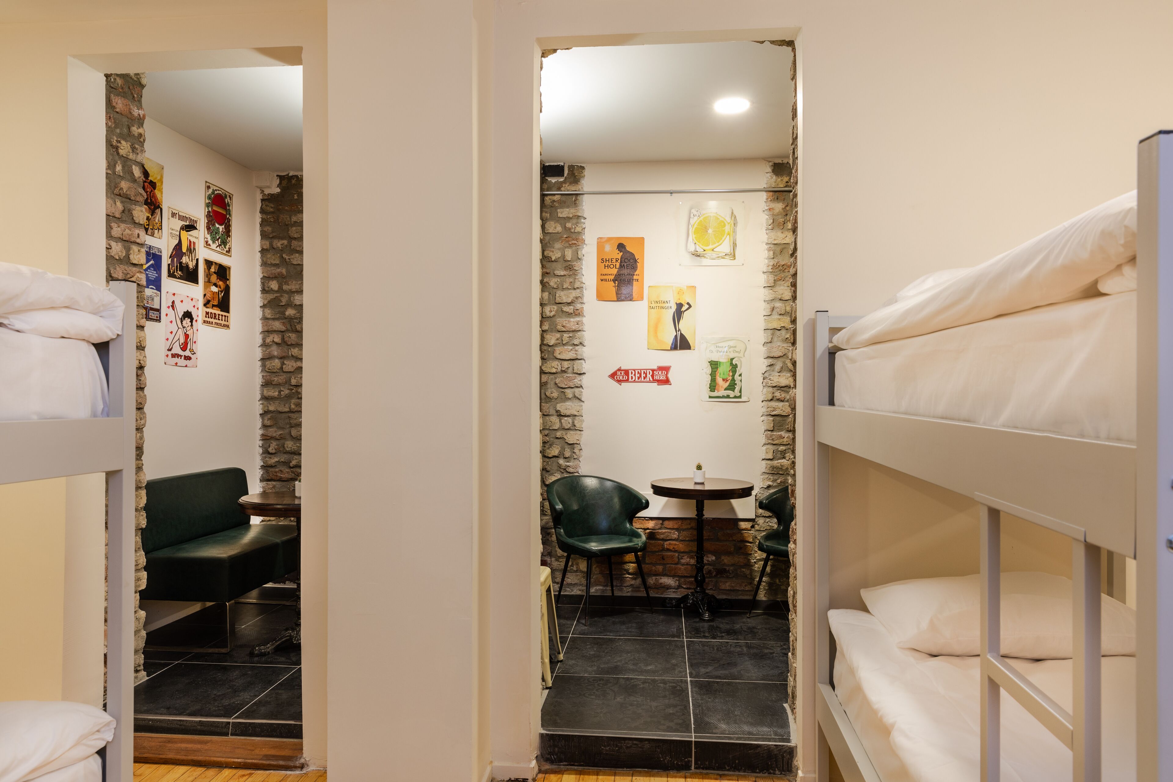 A dormitory room with bunk beds, a small seating area with a table, and a brick wall.