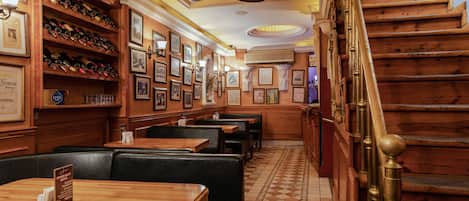 A restaurant interior with wooden tables and booths, a staircase with brass railings, and a ceiling fan.