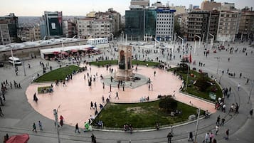 A public square with a central monument, surrounded by buildings and people.
