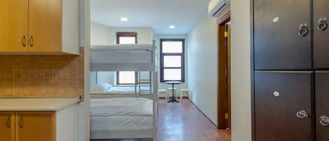 A compact hotel room with a bunk bed, wooden cabinets, a kitchenette, and a large wardrobe.