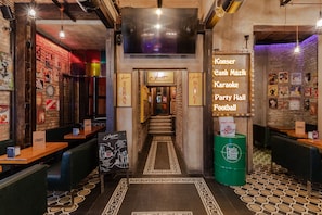 A restaurant interior with a brick wall, wooden tables, and a central staircase. Signs indicate a karaoke and party hall. - Sanat Hostel Taksim (Istanbul)