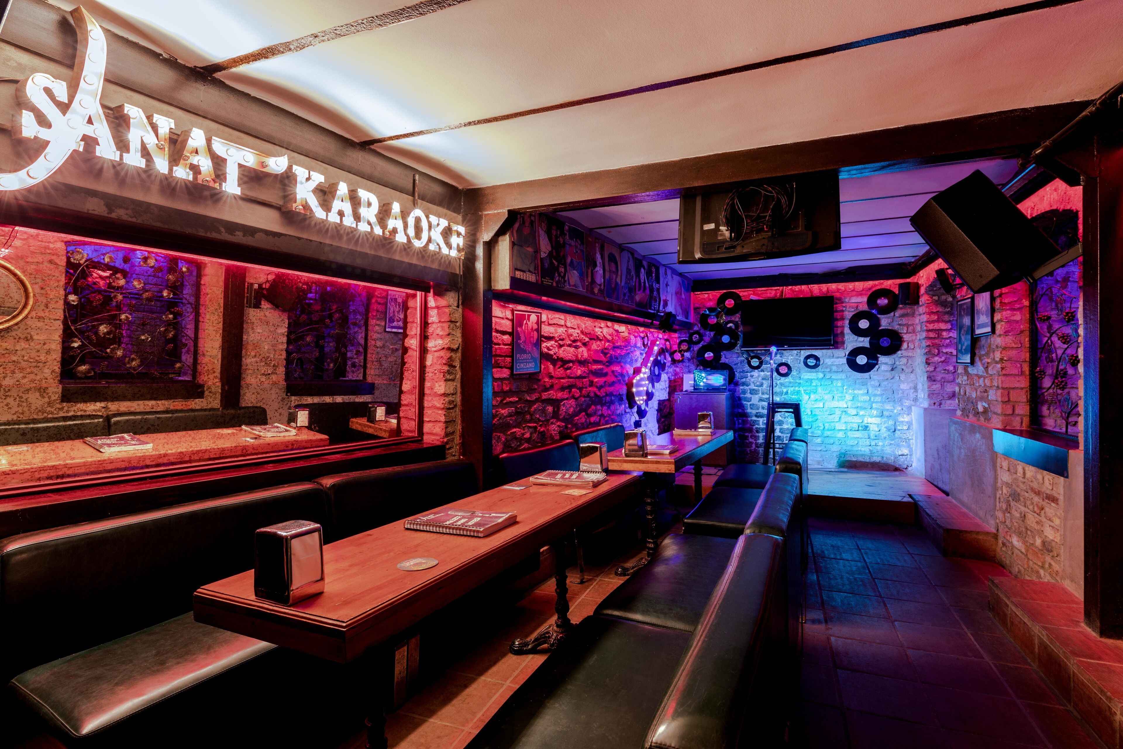 A karaoke bar with wooden tables and benches, a brick wall, and a neon sign.