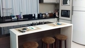 Moderni keittiö, jossa on keskeinen keittiösaareke, baarituolit, mikroaaltouuni ja jääkaappi.