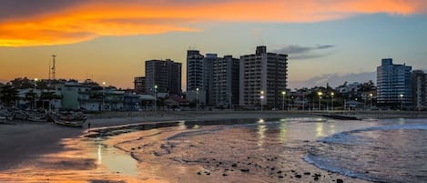 A coastal cityscape at sunset with buildings and a beach.