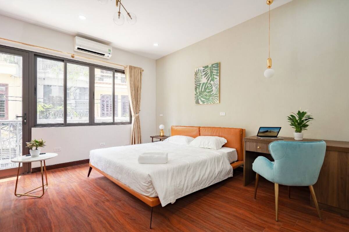A hotel room with a bed, a desk, a chair, a potted plant, and a window with curtains.