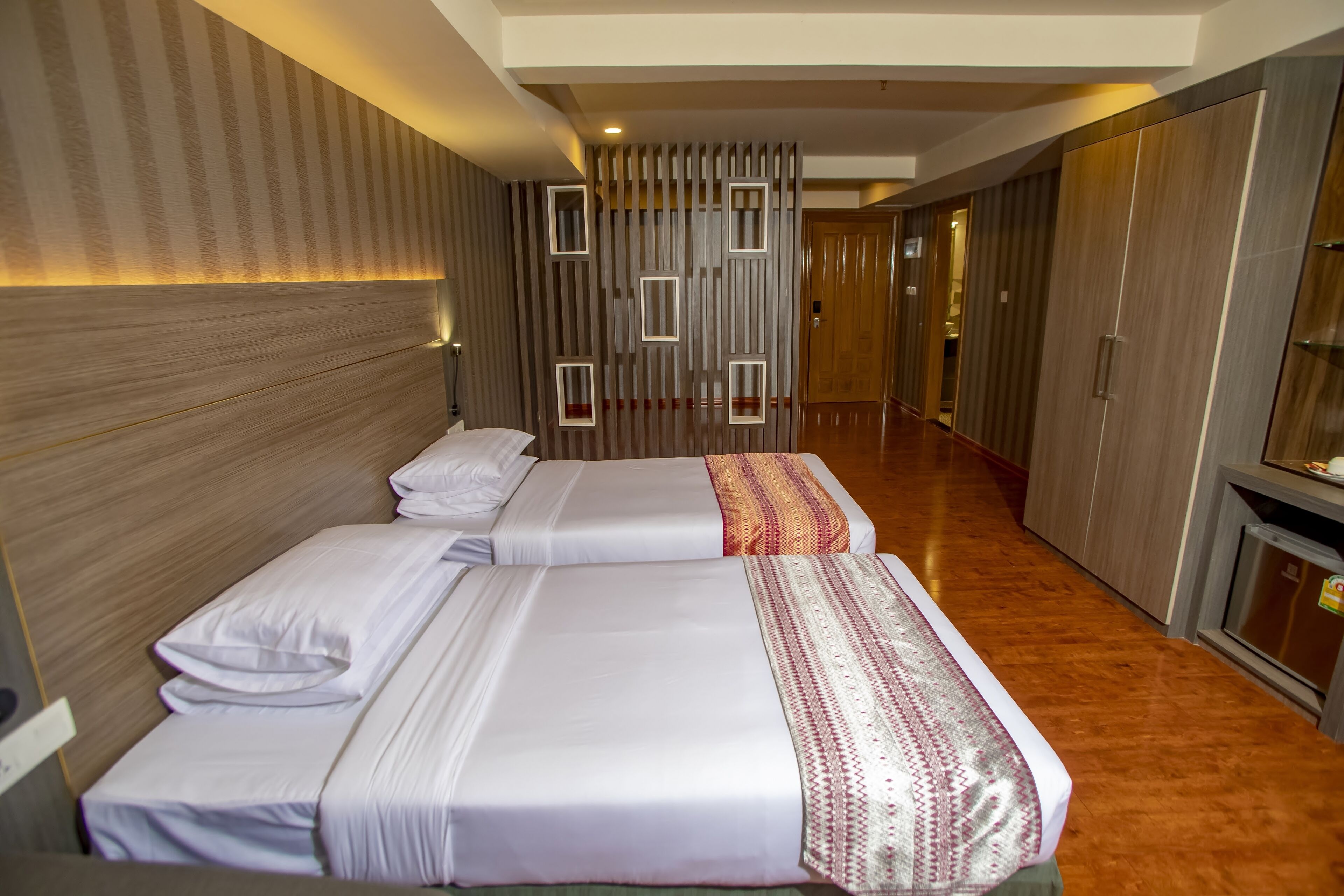 Une chambre d’hôtel avec deux lits, une tête de lit en bois, un panneau décoratif mural et une armoire.
