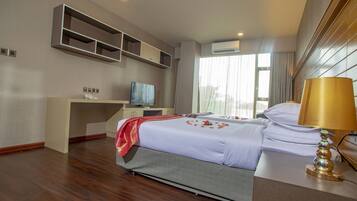 Habitación de hotel con cama, escritorio con televisor, lámpara y ventana con cortinas.