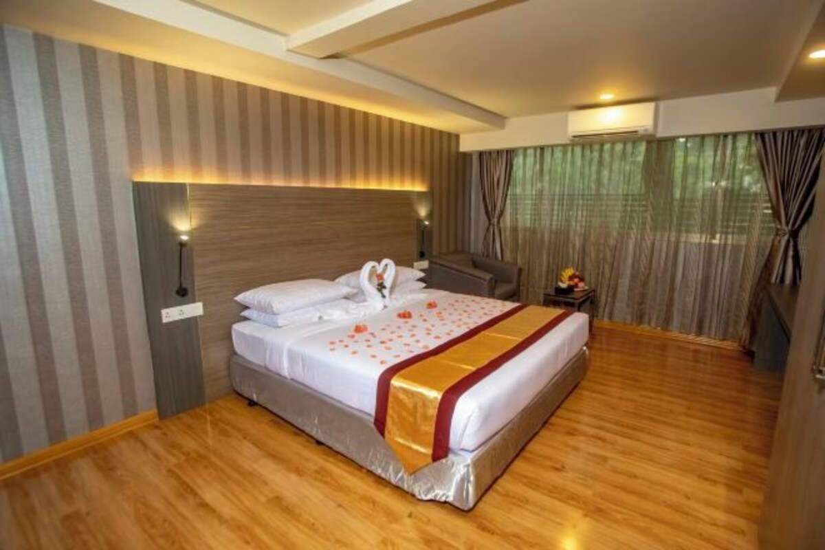 A hotel room with a large bed, a wooden floor, a striped wall, and a window with curtains.