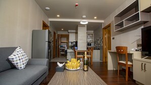 En moderne stue med en grå sofa, et sofabord med en flaske og bananer, samt et spiseområde med et træbord og stole.