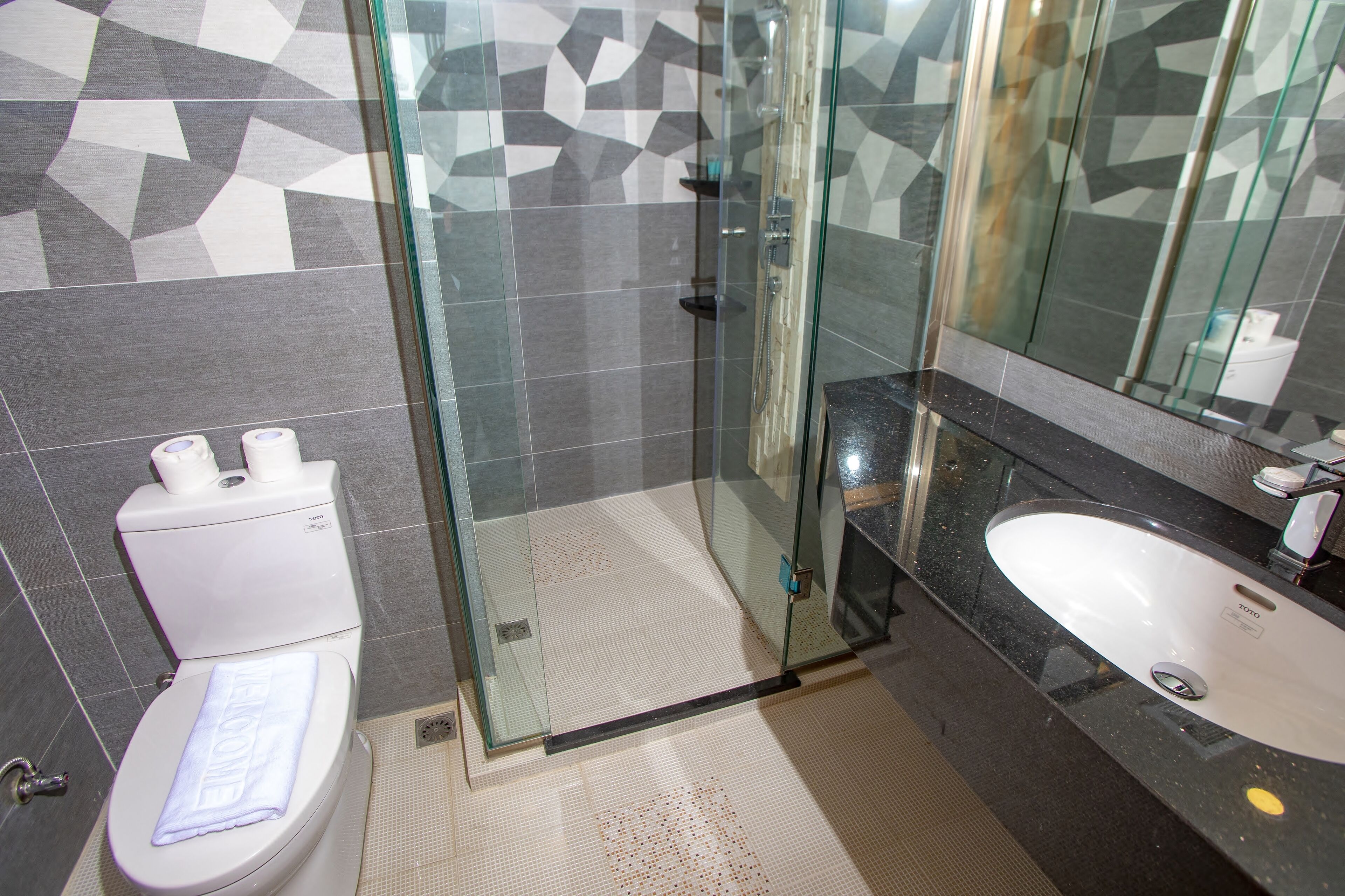 Un baño moderno con cabina de ducha de vidrio, inodoro blanco y encimera negra con lavabo.
