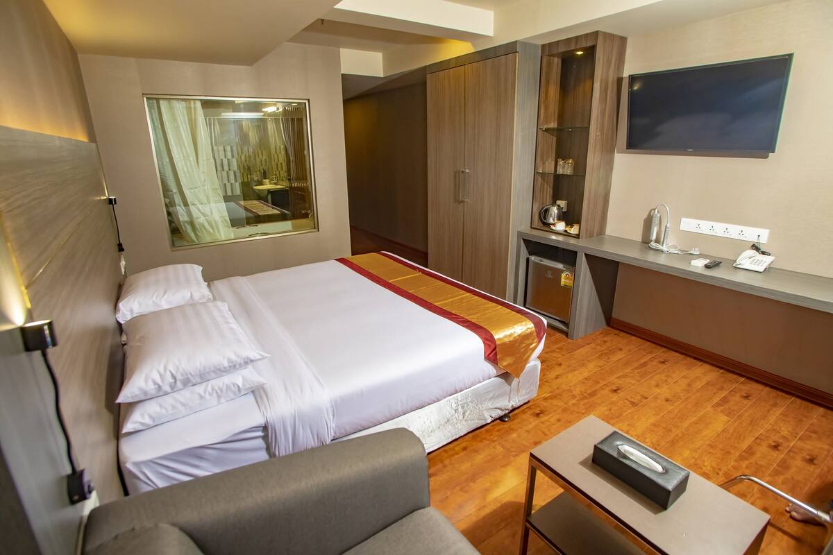 A hotel room with a large bed, a desk with a flat-screen TV, a mirror, and a wardrobe.