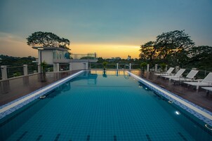 Una piscina con sillas de descanso y un edificio pequeño, rodeada de árboles y vistas al atardecer.