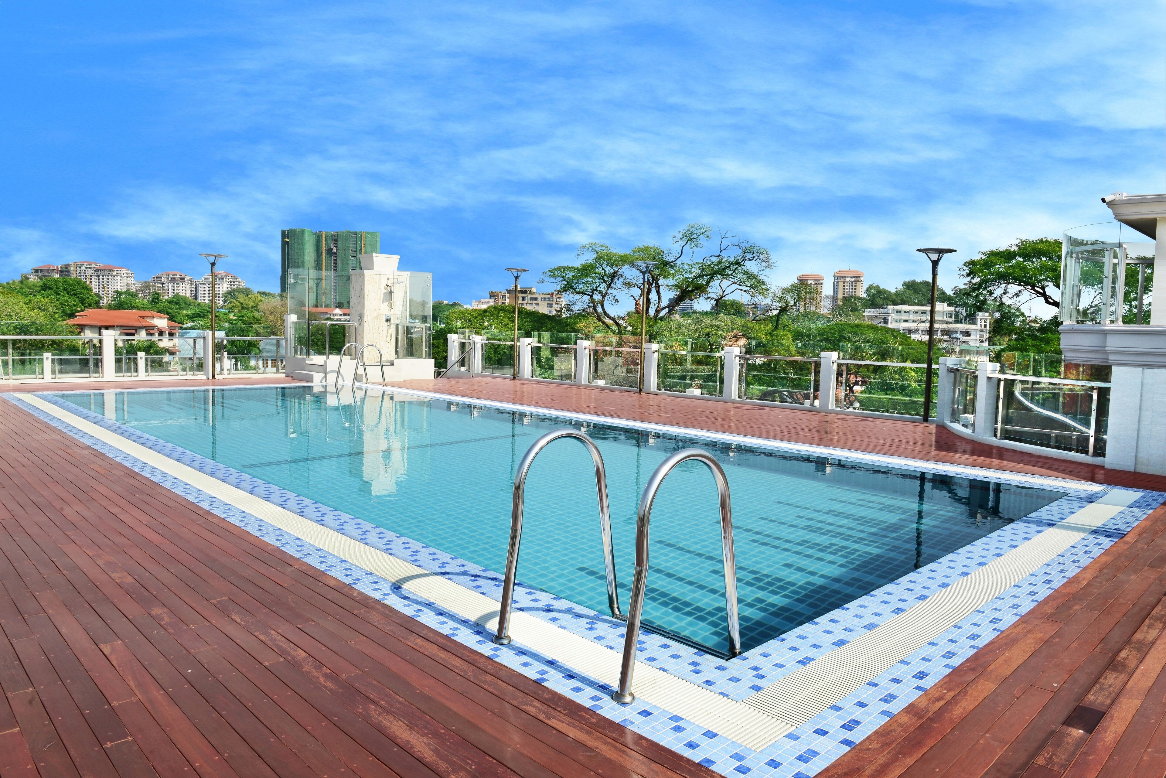 A swimming pool with metal ladders, surrounded by a wooden deck and a glass railing.