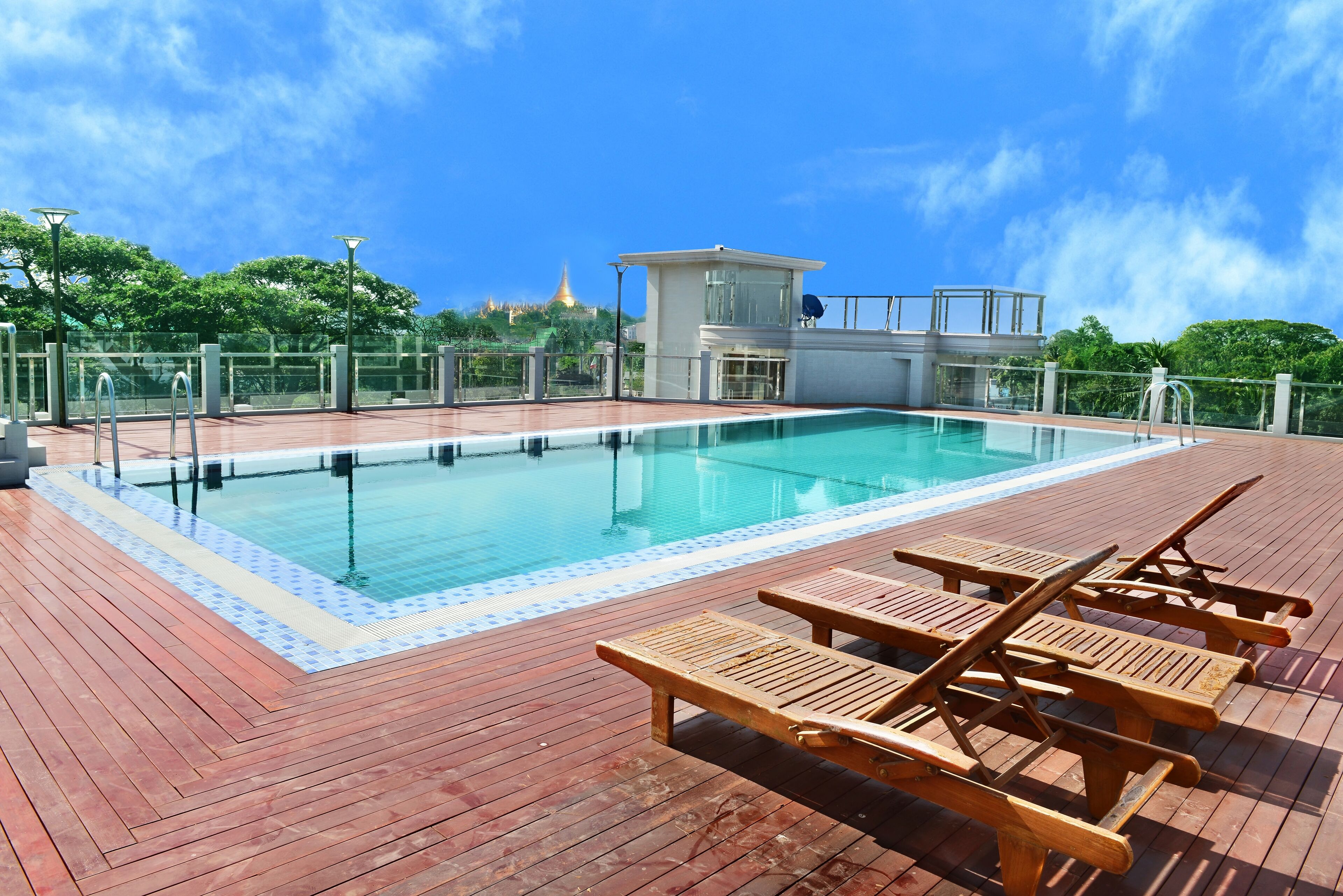 Una piscina con sillones de madera y un edificio pequeño al fondo.
