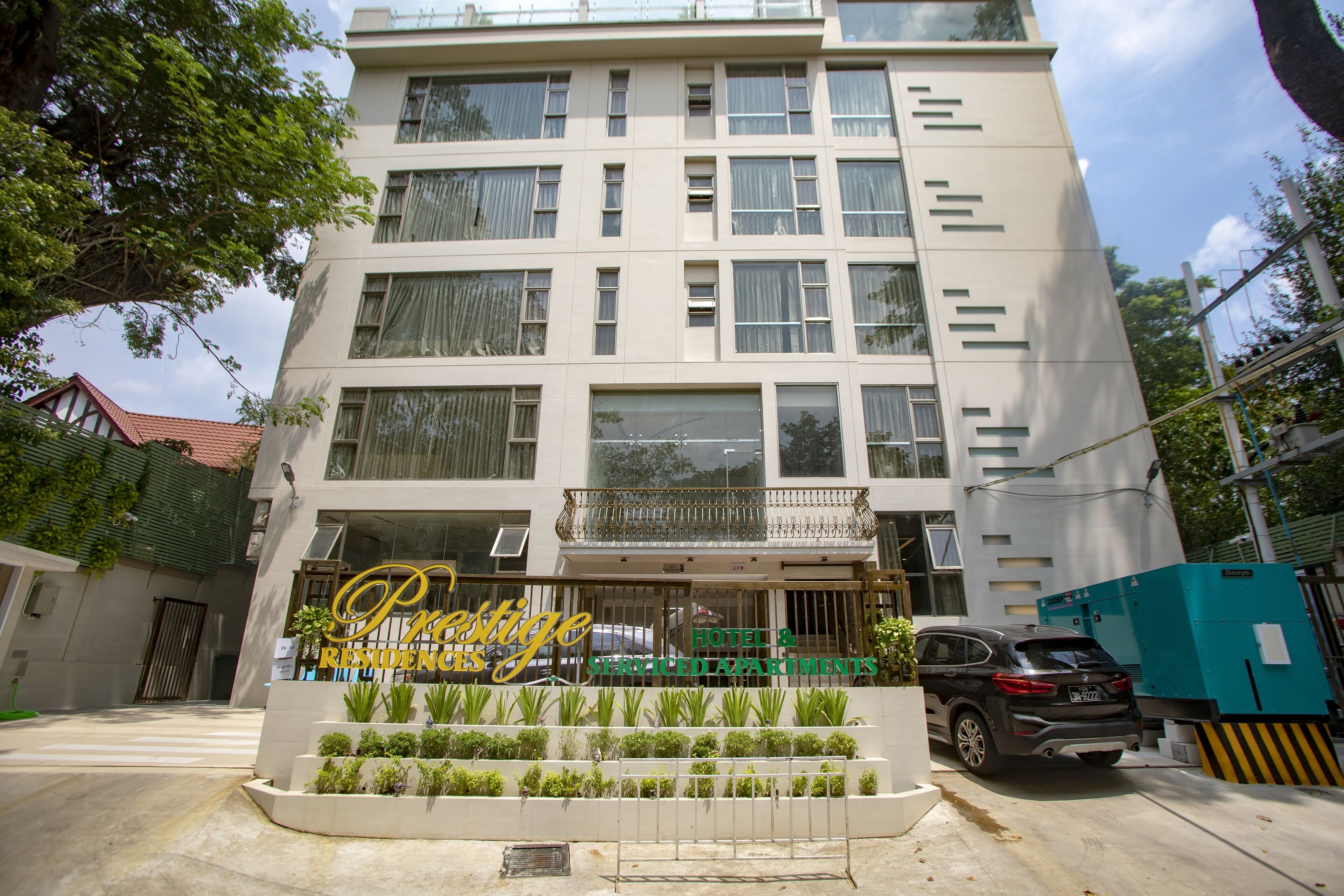 A multi-story hotel with a balcony on the second floor, a sign reading "Prestige Residences," and a parked car in front.