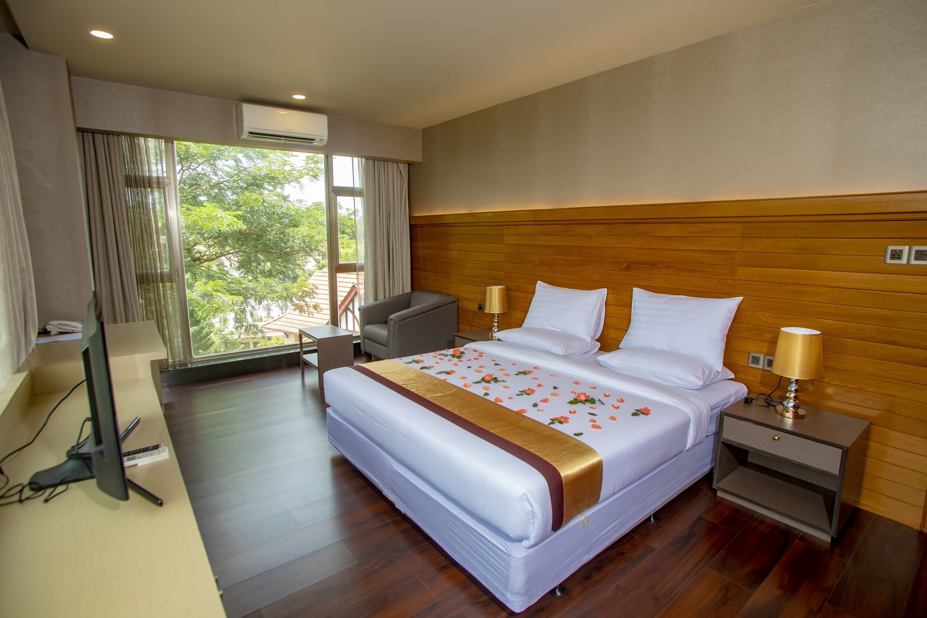 A hotel room with a large bed, a desk with a computer, and a window with curtains.