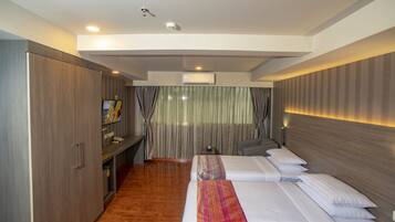 A hotel room with a wooden floor, a bed with white bedding, a desk with a chair, and a wardrobe.