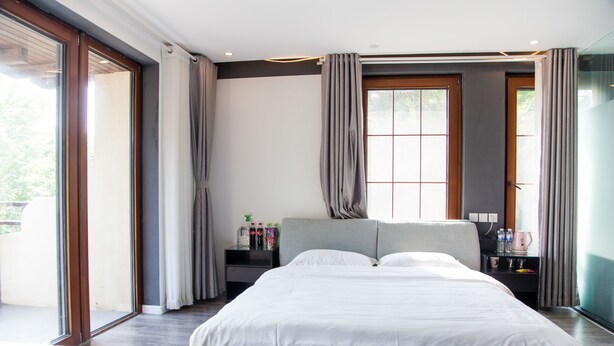 A modern bedroom with a large bed, a nightstand with toiletries, and a view through a glass door. - Villa Haixin (Qingdao)