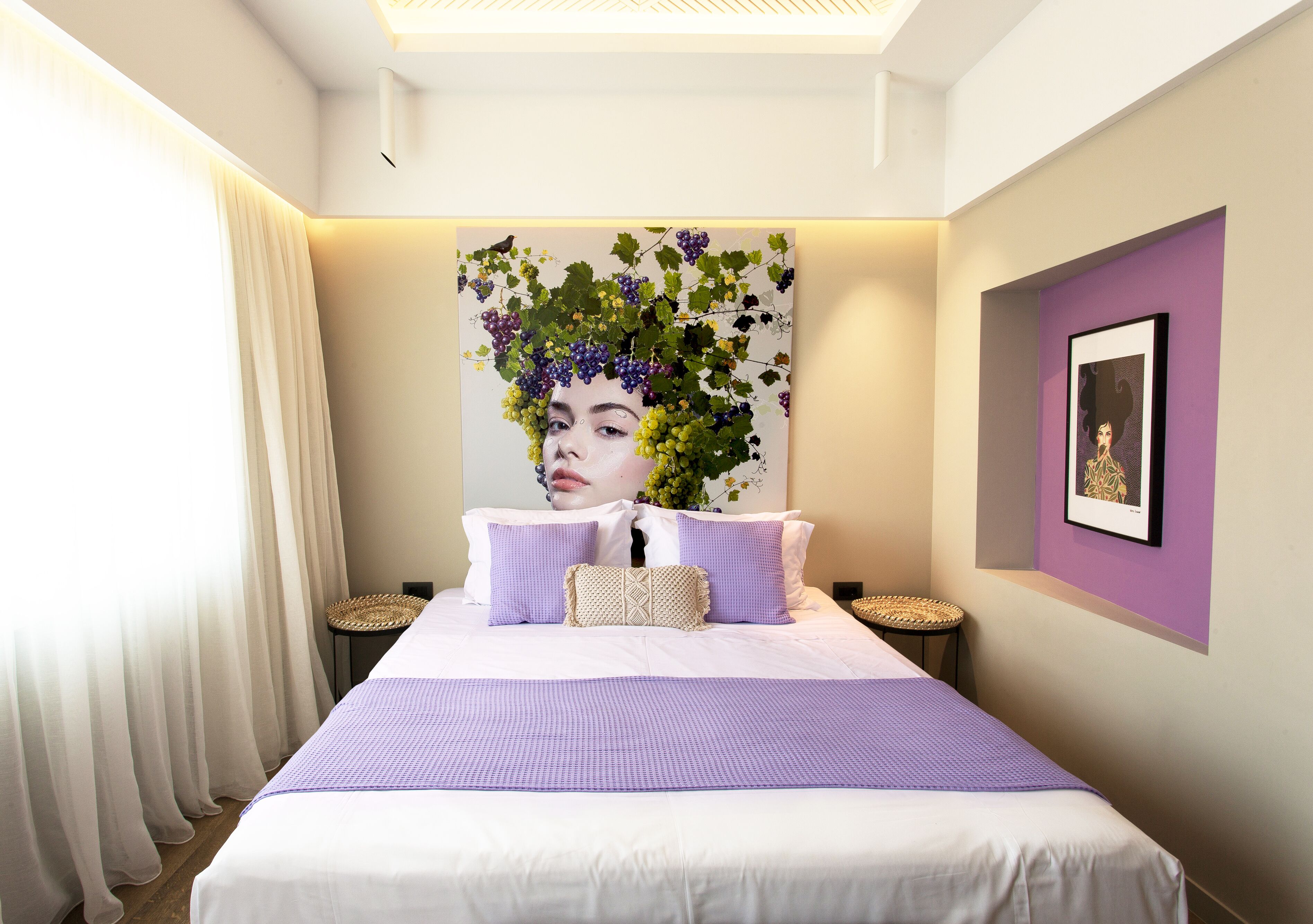 Una camera da letto con un letto grande, biancheria bianca, una coperta viola e un'opera d'arte a parete.